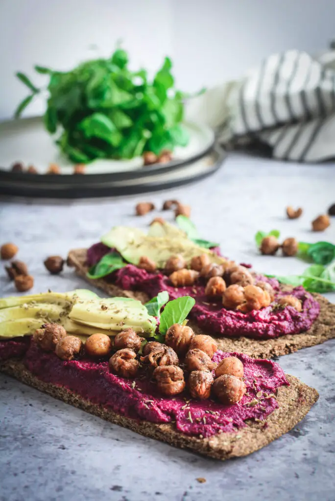 Beet Hummus on two flat breads topped with avocado and crispy chickpeas