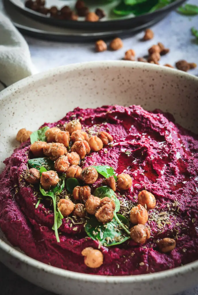 Beet Hummus in bowl shot from the side with crispy chickpeas, greens and oregano