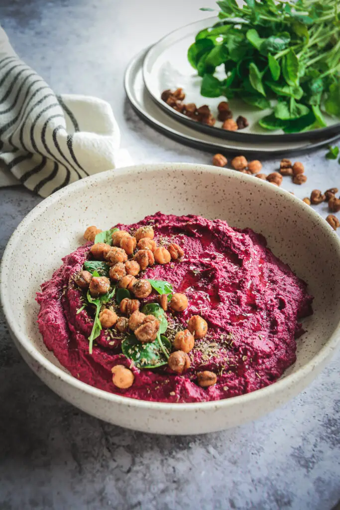 Beet Hummus in bowl shot from the side topped with crispy chickpeas and greens