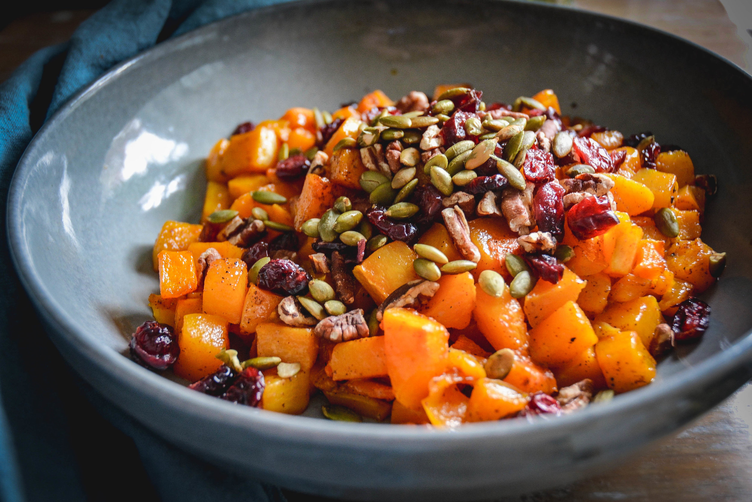 orange squash cubbed with seeds and red dried cranberries in a bowl