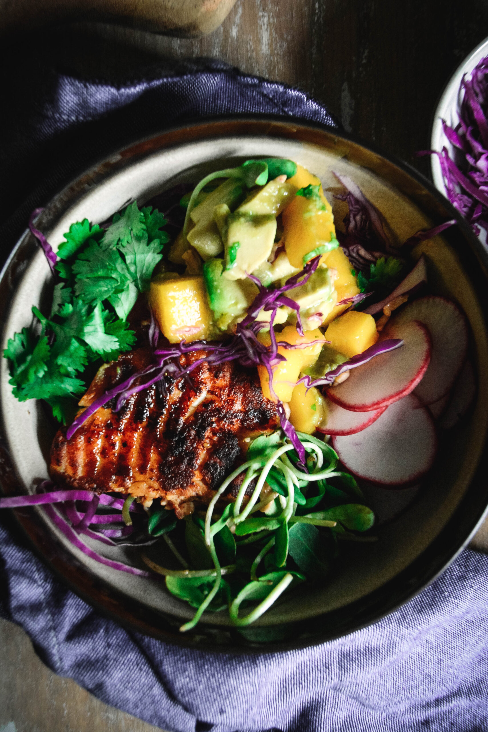 grilled fish, avocado, radish slices, cilantro and sprouts in a bowl
