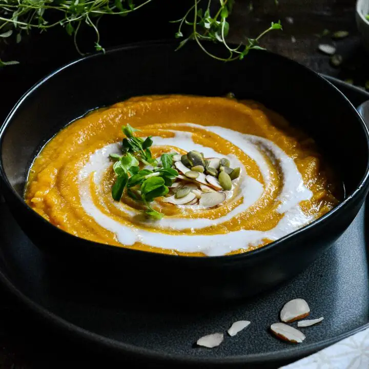 Butternut squash soup in black bowl with creamy swirl, pumpkin seeds and almond slivers.