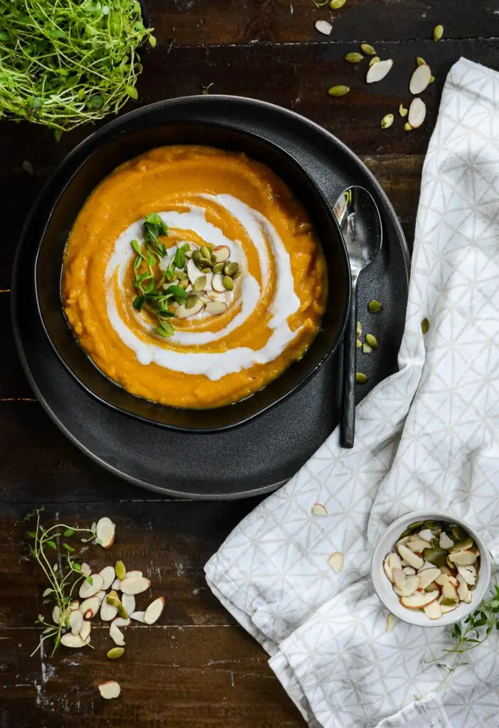 Squash soup in bowl on a plate with spoon, napkin and almond and pumpkin seeds.