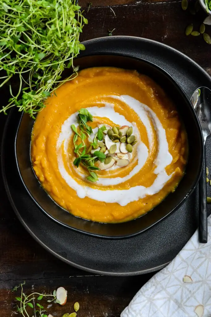 Squash soup in bowl with coconut cream swirl and pumpkin seeds