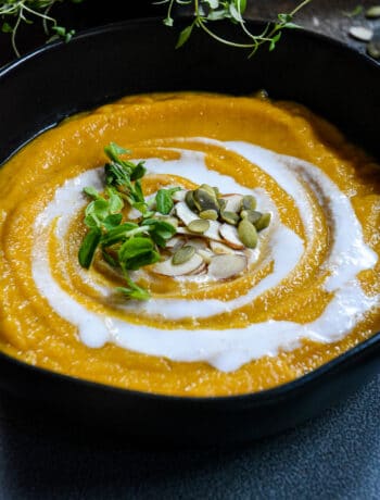 Butternut squash soup in black bowl with creamy swirl, pumpkin seeds and almond slivers.