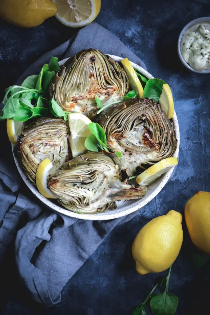 roasted artichoke halves with lemon slices in bowl 