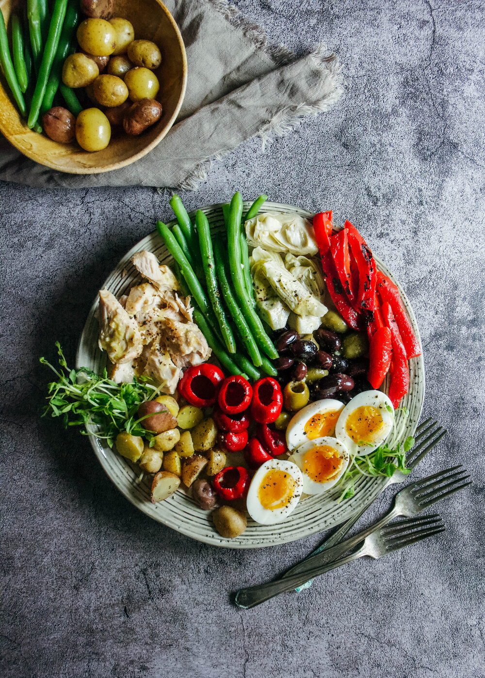 soft boiled eggs, cooked potatoes, tuna, beans, red peppers, olives on a plate