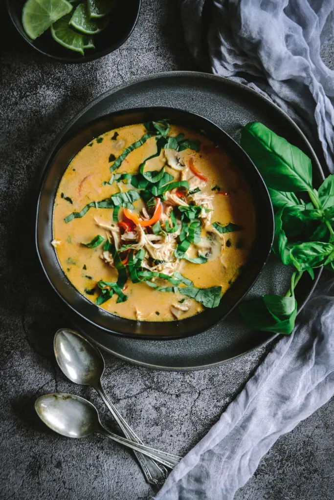 Thai coconut soup in bowl with plate, napkin and basil