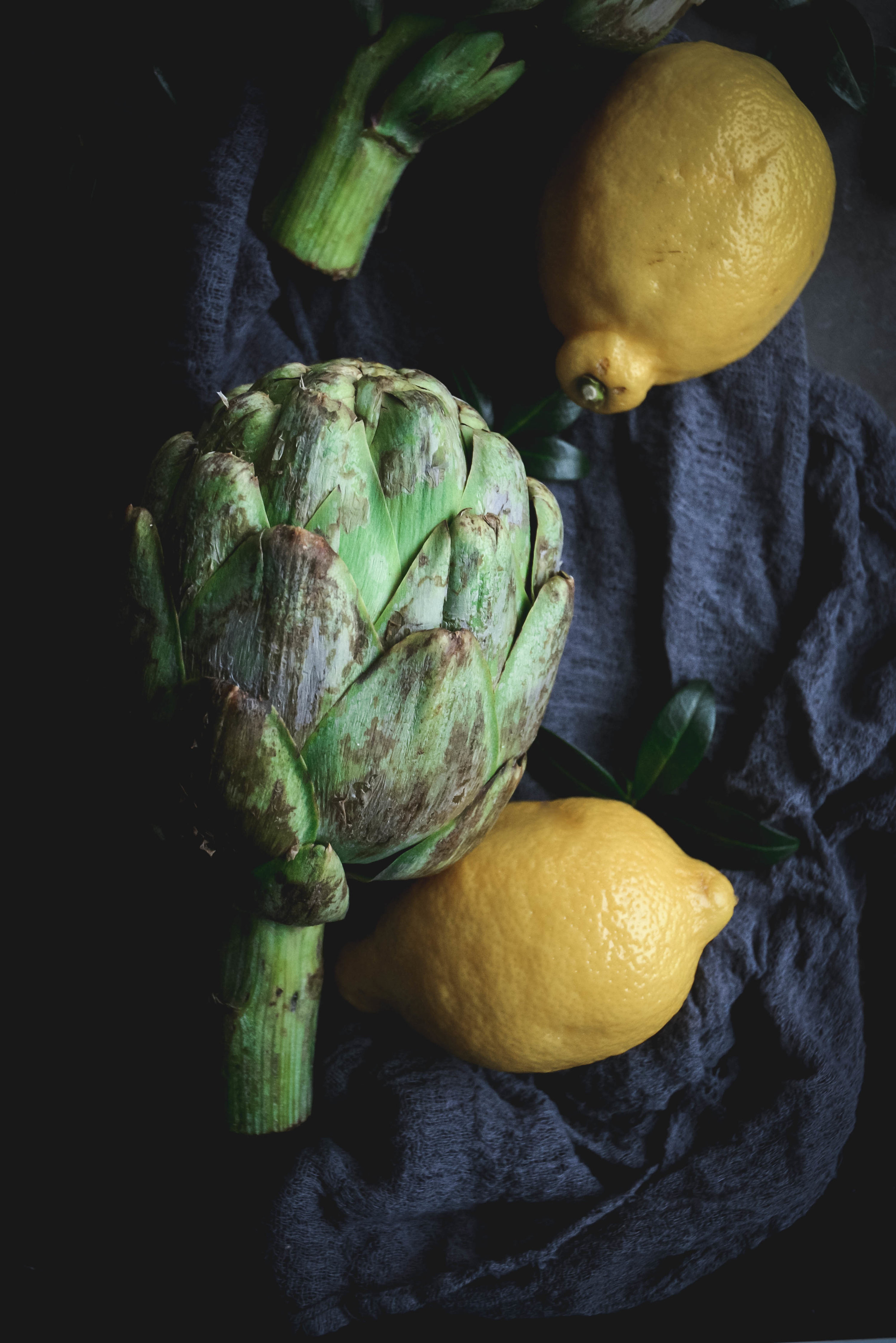 artichoke on dark napkin with whole lemons