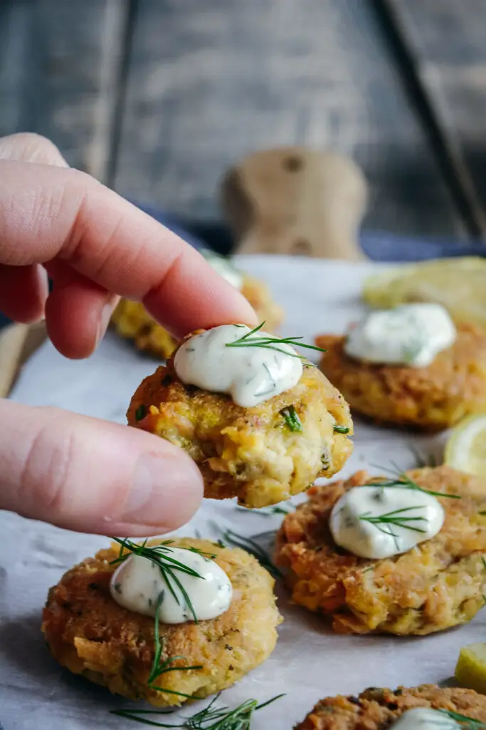 tuna and chickpea bites on cutting board. one held between fingers with mayo and dill