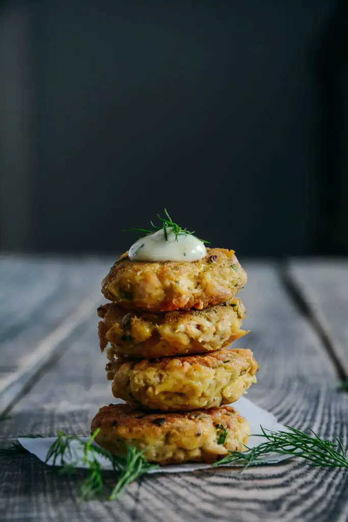 tuna and chickpea bits stacked on table topped with lemon mayo sauce and dill