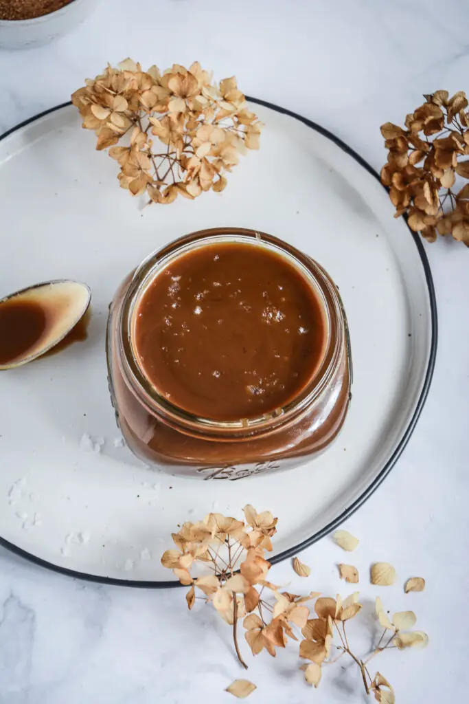 caramel sauce in jar on plate with spoon next to it