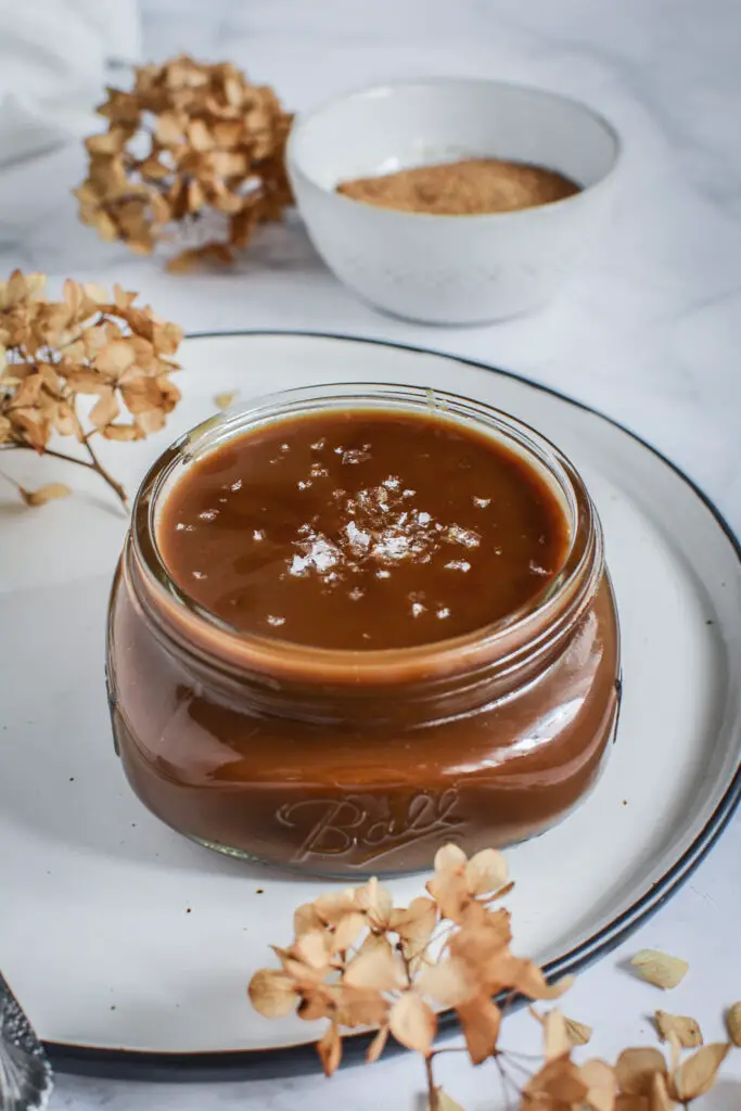 salted caramel sauce in jar on white plate with flaked salt