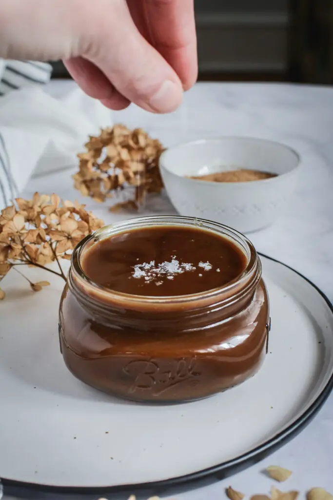 salt being added to caramel sauce, bowl of coconut sugar and dried flowers