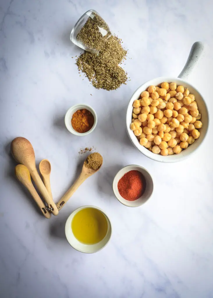 olive oil, spices in bowl, oregano and chickpeas peeled in bowl with wooden spoons on table