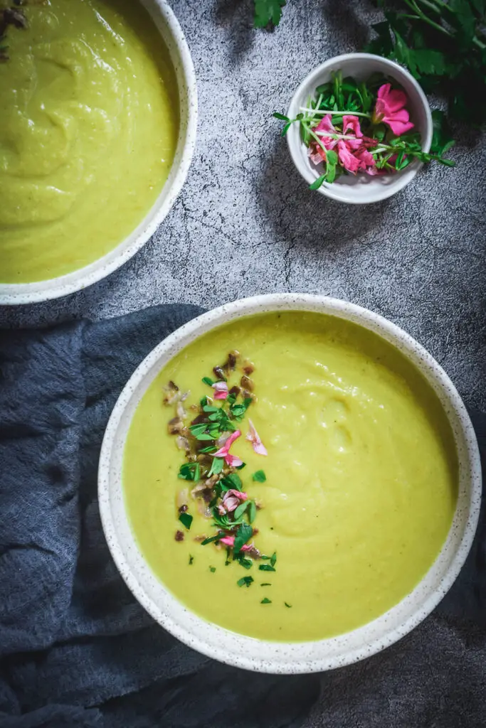 golden cauliflower soup in bowl with parsley, edible flowers bacon