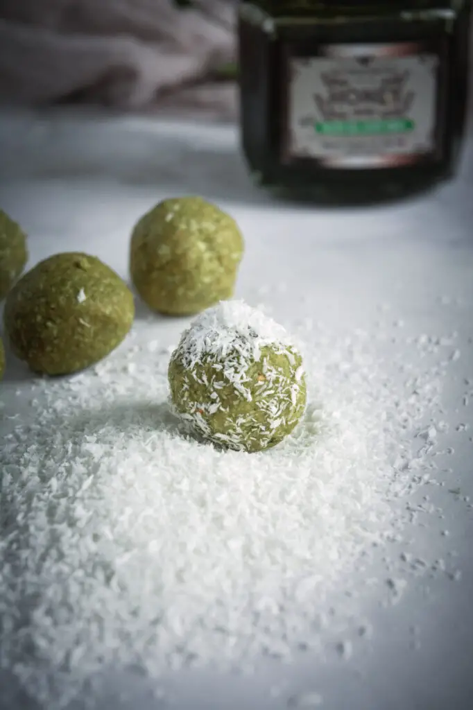 Coconut Cashew Matcha Energy Bites in coconut flakes, honey jar in background