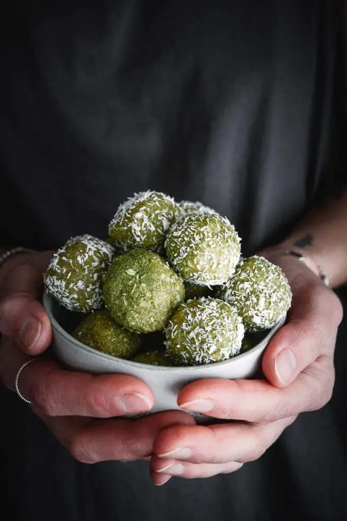 matcha balls covered with shredded coconut in bowl, held in hands