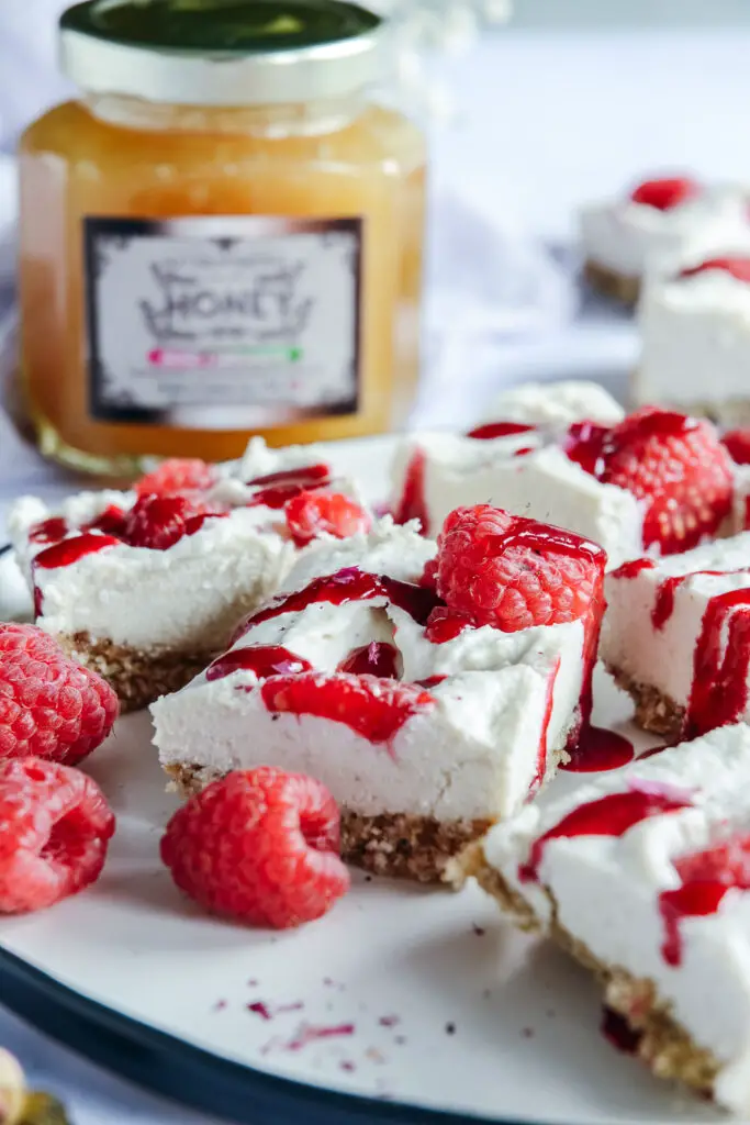 Vegan Raspberry Cheesecake Bites with Rose Cardamom Honey on plate with jar of honey in the background 