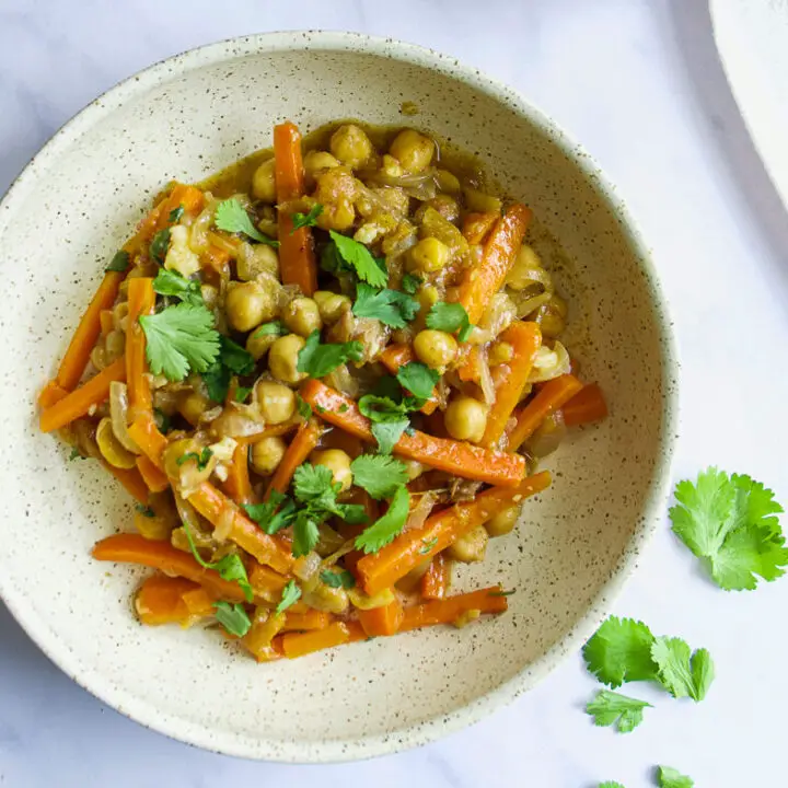 Moroccan Chickpea Tagine with Preserved Lemons in bowl with cilantro and preserved lemons in bowl in background and large tagine clay pot