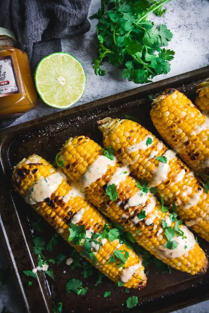 Grilled Corn with Spicy Habanero Honey Mayo drizzled over the corn with lime slice and cilantro