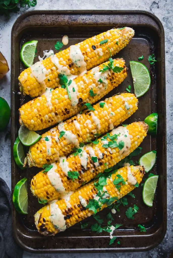 Grilled Corn with Spicy Habanero Honey Mayo on tray with lime and mayo drizzle 