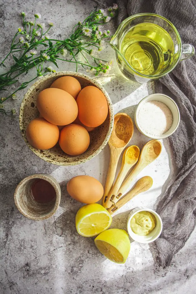 Eggs in bowl, olive oil in clear glass container, salt in bowl, wooden spoons, lemons, green and white flowers, napkin