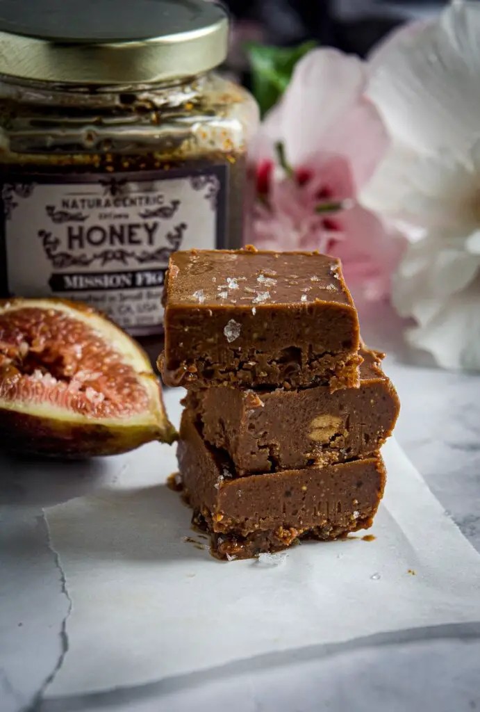 Vegan chocolate fudge stacked in front of jar of honey with fig next to it