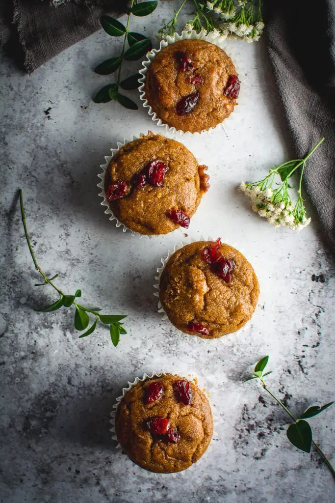 Healthy Grain-Free Cranberry Pumpkin Spice Muffins on table with greens, flowers and napkin