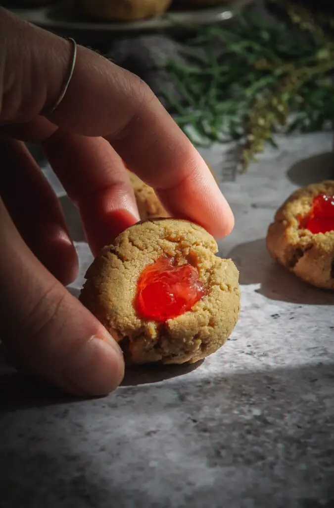 Almond Flour Cardamom Peanut Butter Thumbprint Cookies in hand being hit by streaming sunlight. 