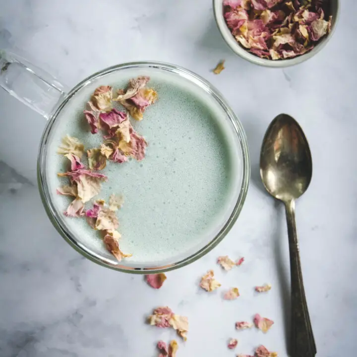 Cardamom Moon Milk in mug with spoon and a small bowl of dried rose petals
