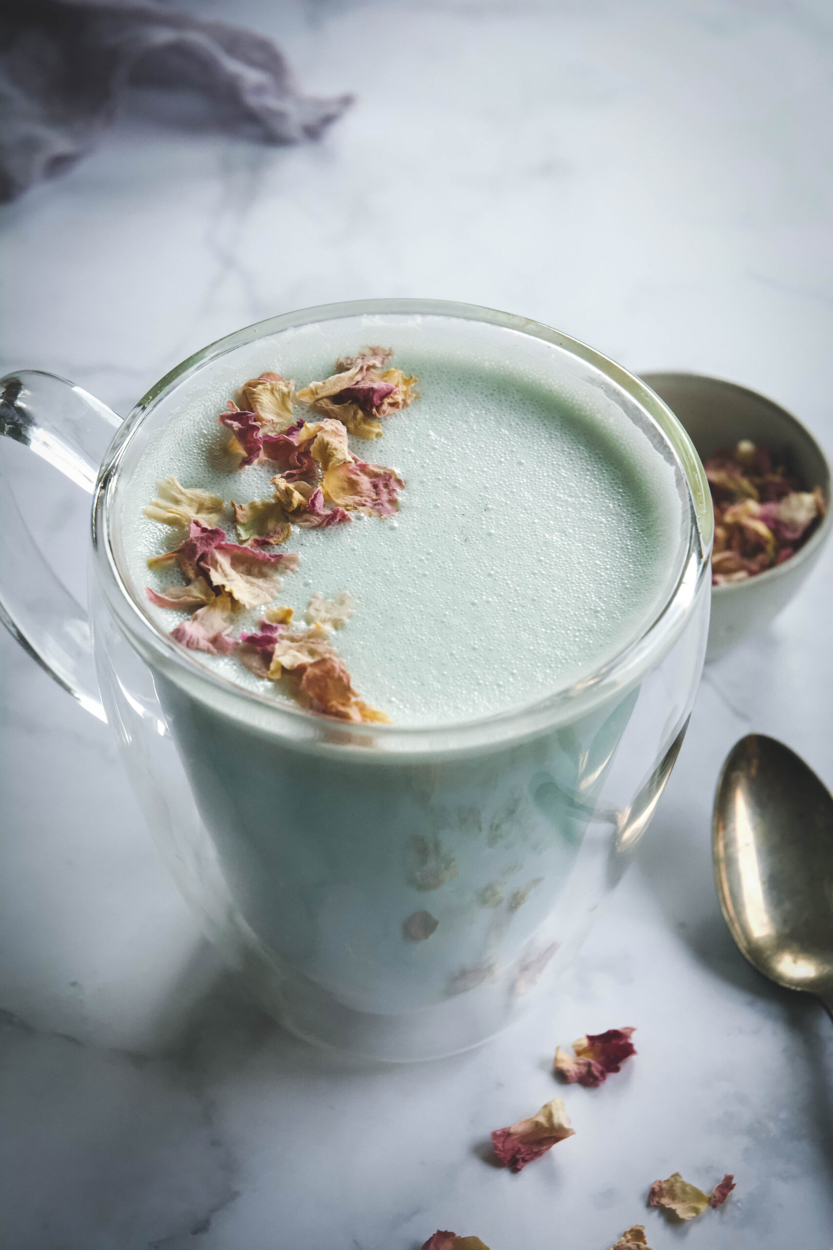 Cardamom Moon Milk in mug with spoon and a small bowl of dried rose petals
