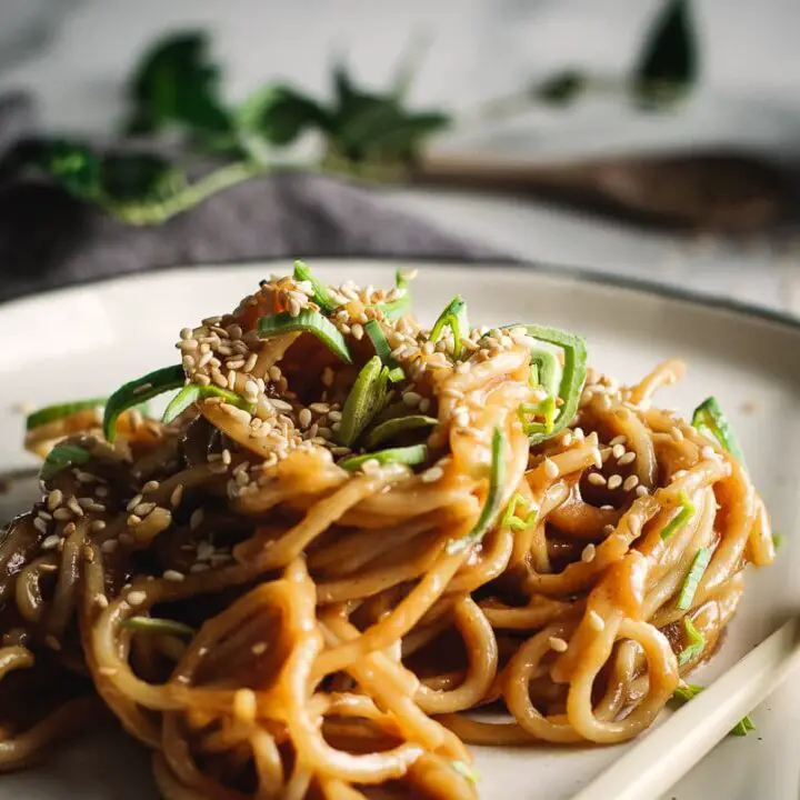 Sesame peanut noodles on plate sprinkled with sesame seeds and sliced green onion