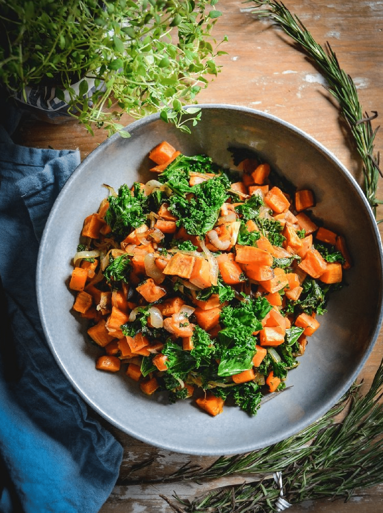 Sweet Potatoes with Kale and Caramelized Onions on grey plate with herbs and blue napkin