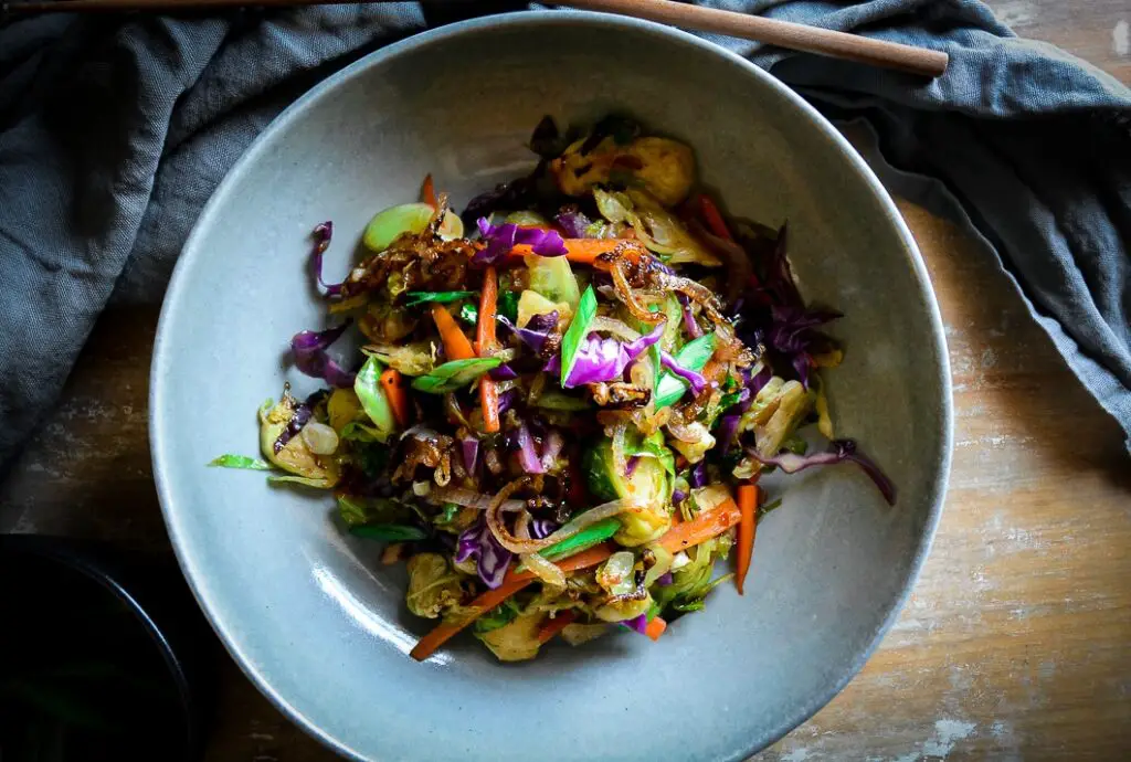cooked shaved brussels sprouts with carrots and purple cabbage and scallions on grey plate