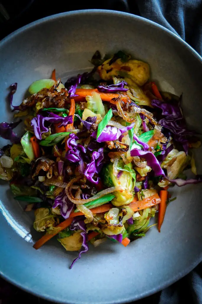 cooked shaved brussels sprouts with carrots and purple cabbage and scallions on grey plate