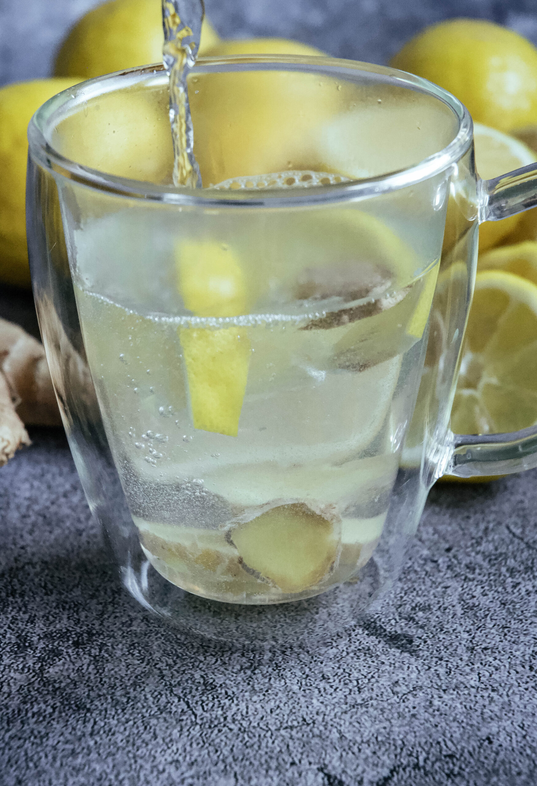 Clear cup with lemon slices, water being poured into it. 