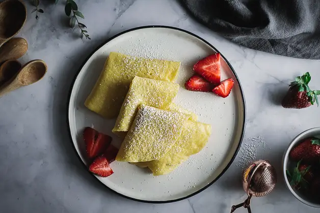 crepes in triangle shapes on plate with strawberries, eucalyptus