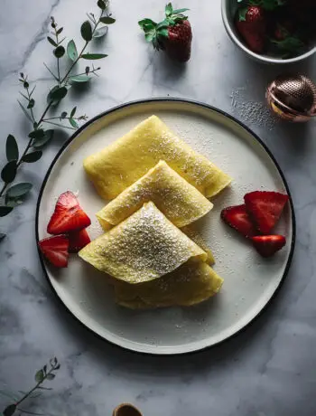 crepes in triangle shapes on plate with strawberries, eucalyptus