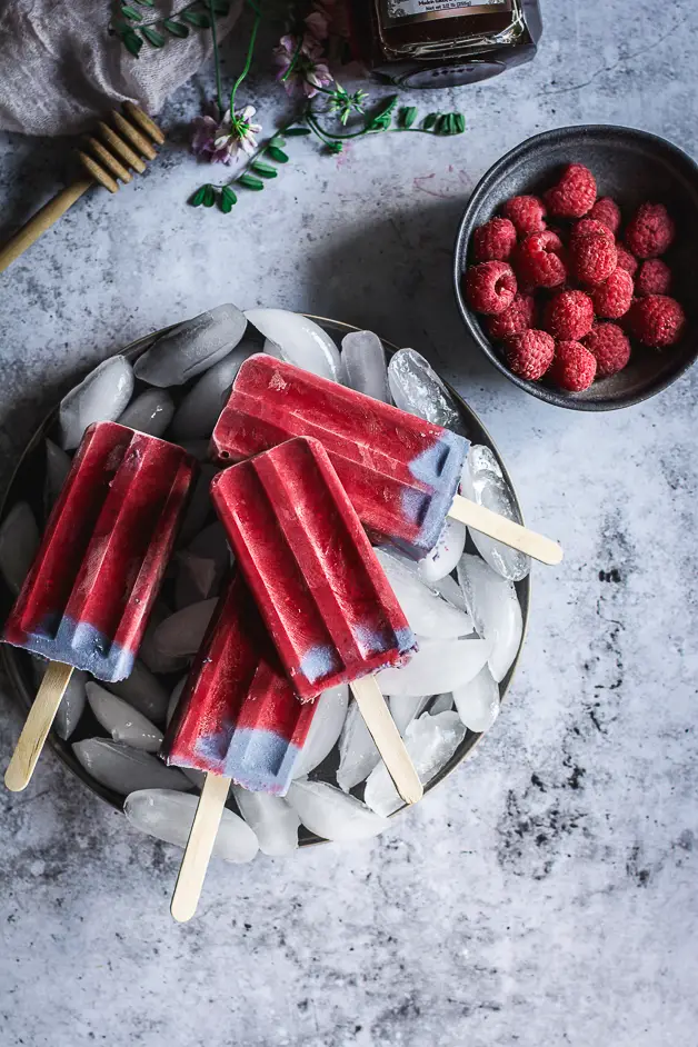 raspberry popsicles on a plate of ice cubes with a bowl of raspberries next to it
