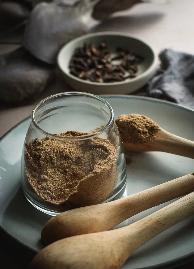 a small jar of spices on a plate with a wooden spoon next to it