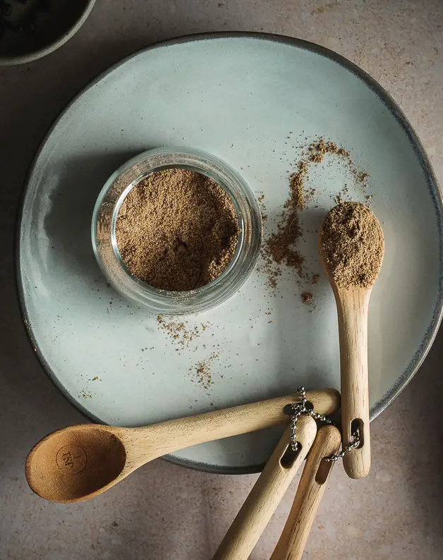 a small jar of spices on a plate with a wooden spoon next to it