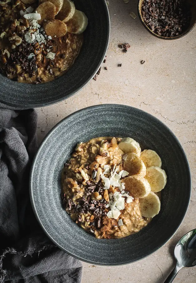 pumpkin oatmeal in blue bowl with bananas, walnuts, coconut flakes and cacao nibs