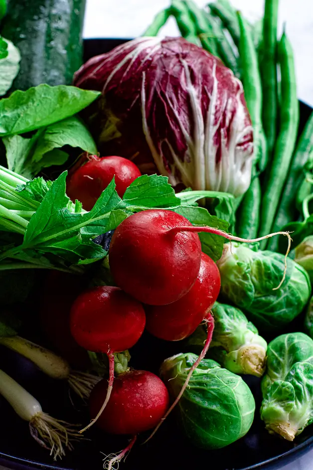 radishes, radicchio, green beans, scallions, brussels sprouts on a black plate