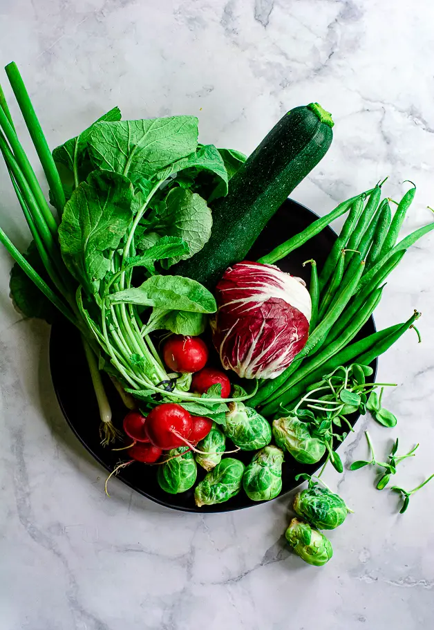 radishes, radicchio, green beans, scallions, brussels sprouts on a black plate