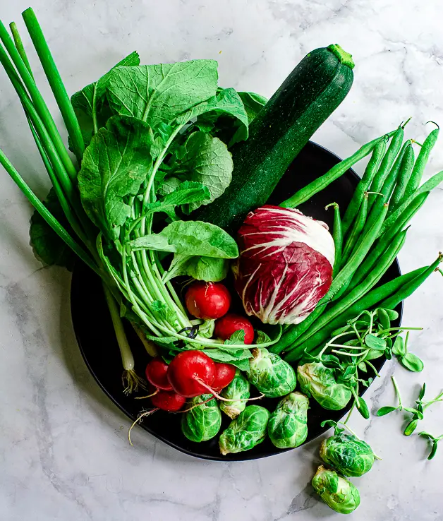 radishes, radicchio, green beans, scallions, brussels sprouts on a black plate