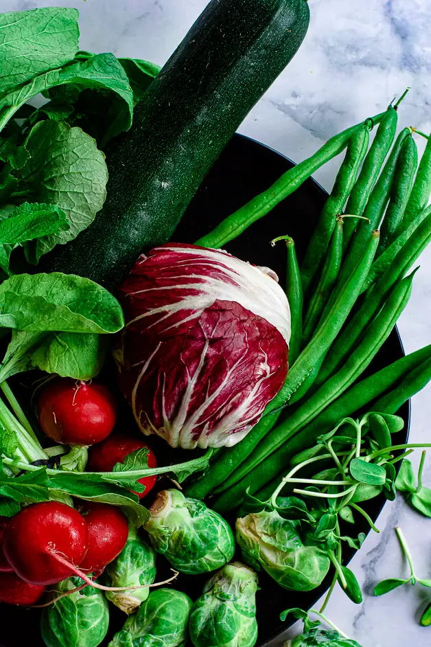 radishes, radicchio, green beans, scallions, brussels sprouts on a black plate