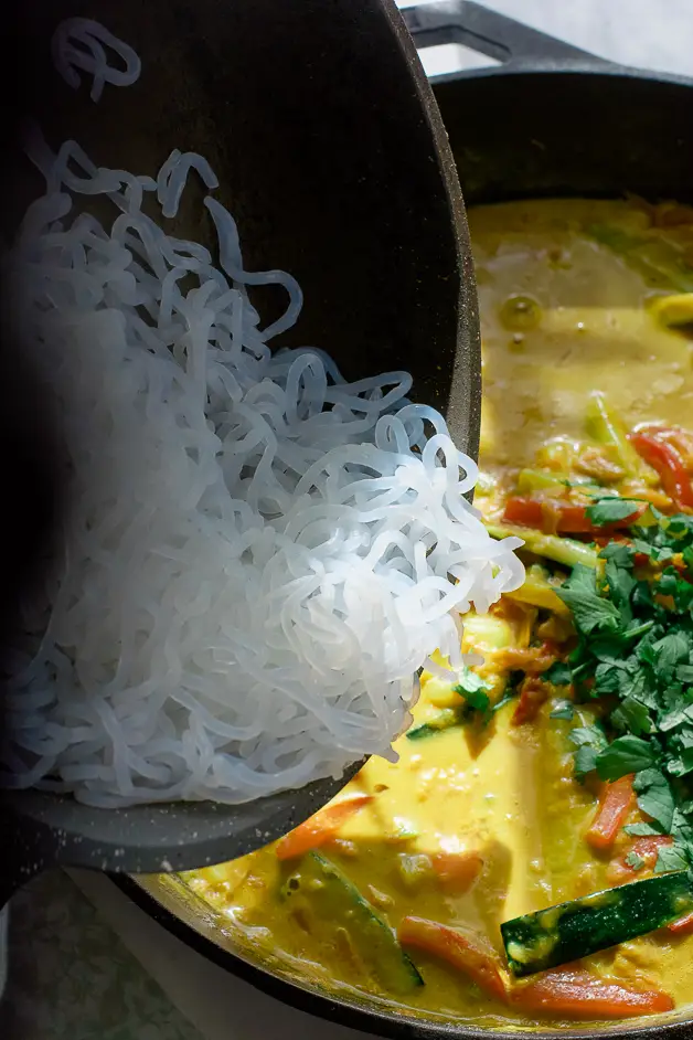 noodles being dumped into peanut vegetable sauce