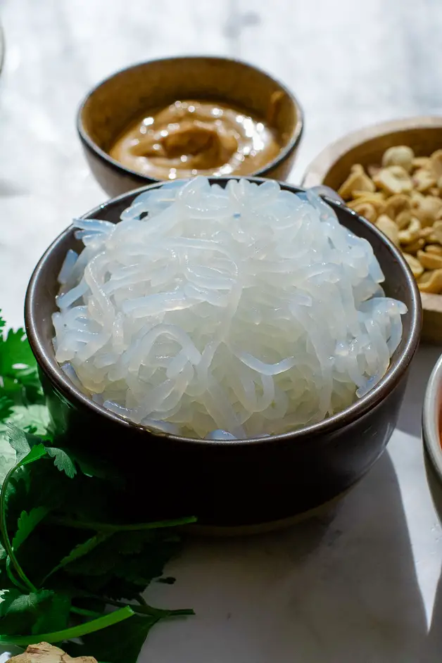 a bowl of noodles, pleanut butter in the background