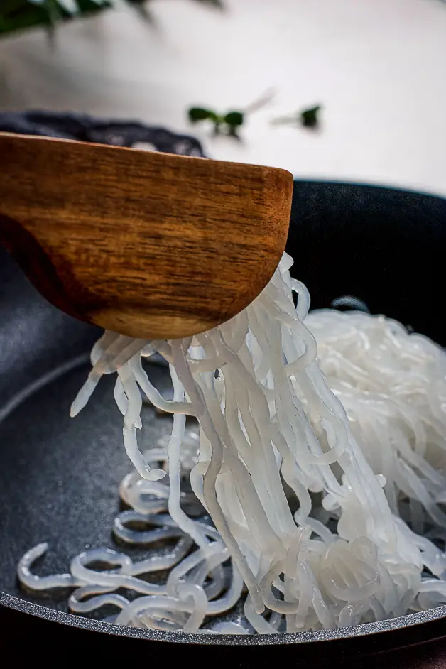 noodles in a frying pan with a tongs